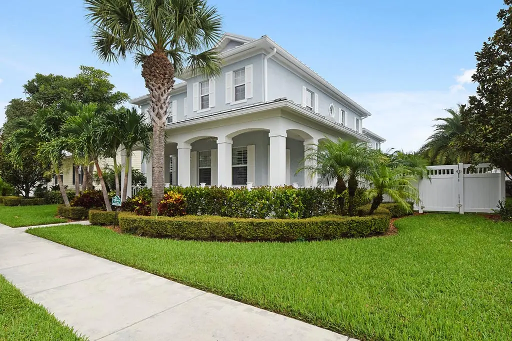 A white house with palm trees and bushes around it.